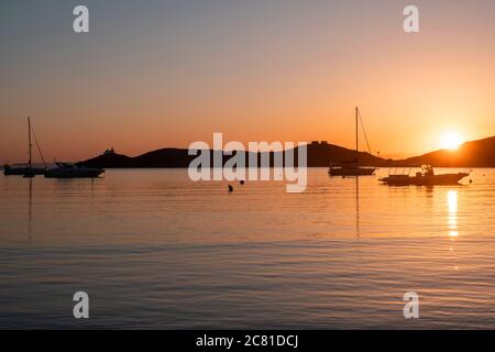 Kea island, Greece. Sunset orange color over sea water. Boats anchored at Vourkari port, golden reflections on the rippled water, Aegean Mediterranean Stock Photo