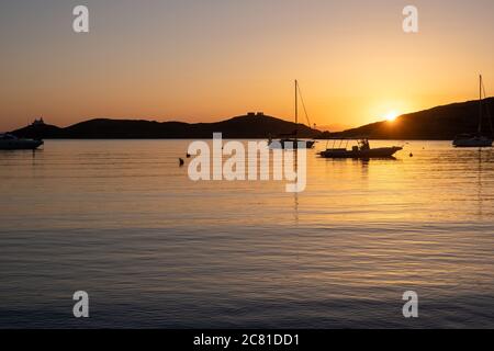Kea island, Greece. Sunset orange color over sea water. Boats anchored at Vourkari port, golden reflections on the rippled water, Aegean Mediterranean Stock Photo