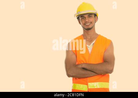 Studio shot of young happy Indian man construction worker smiling with arms crossed Stock Photo