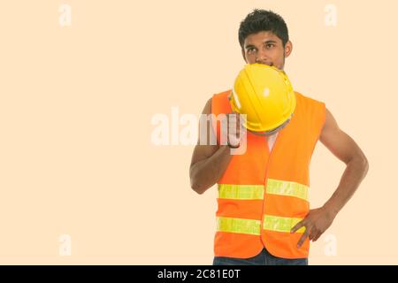 Young handsome Indian man construction worker covering face with safety helmet while thinking Stock Photo