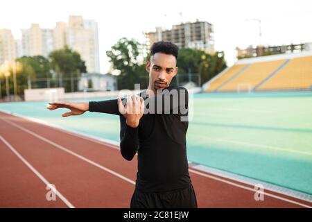 Young serious African American sportsman stretching preparing for run on racetrack at stadium Stock Photo
