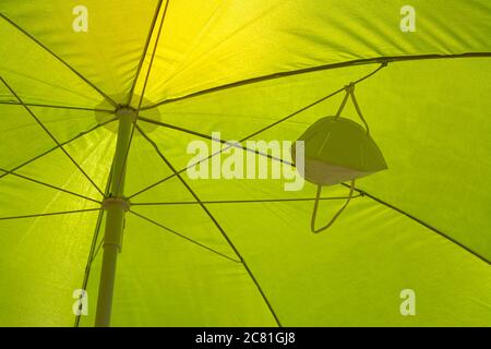Facial mask at the bottom of an umbrella on the beach or in the pool with sunlight. New normal concepts during the pandemic Stock Photo
