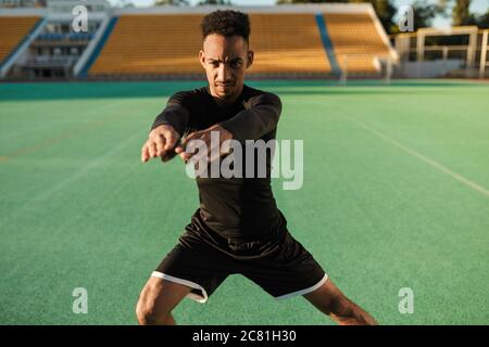Young serious African American sportsman heavily doing exercises during workout at stadium Stock Photo