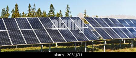 Solar panel collectors in forest, coniferous trees and mountains background, clear sky above, closeup detail Stock Photo