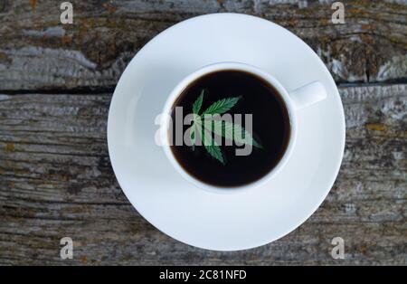 Cannabis coffee - marijuana leaf on coffee cup, top view, rustic wooden background Stock Photo