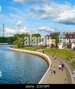 MINSK, BELARUS - JULY 17, 2019: People walking by Svisloch river embankment in bright sunny daytime, green park and city architecture in background Stock Photo