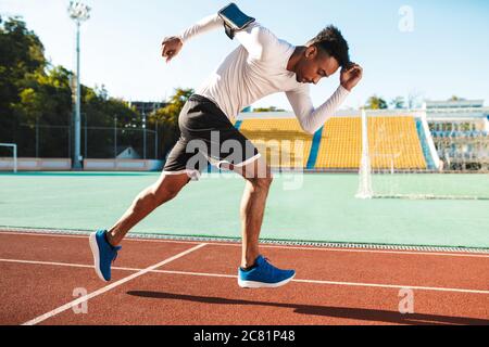 Side view of young attractive African American sportsman running on racetrack at stadium Stock Photo