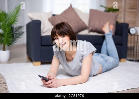young woman or teenage girl lying on the floor with smart phone at home Stock Photo