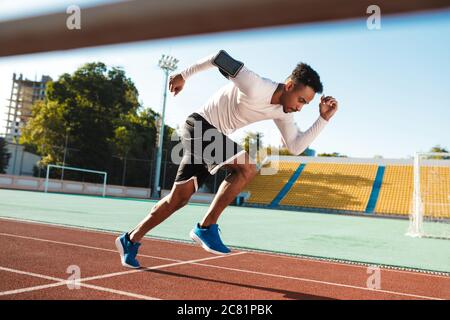Side view of young African American sportsman running on racetrack at stadium Stock Photo