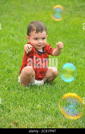 A male toddler sitting on the lawn fascinated by bubbles Stock Photo