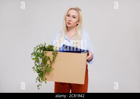 portrait of unhappy business woman holding cardboard box after getting fired from her job, copy space over gray background Stock Photo