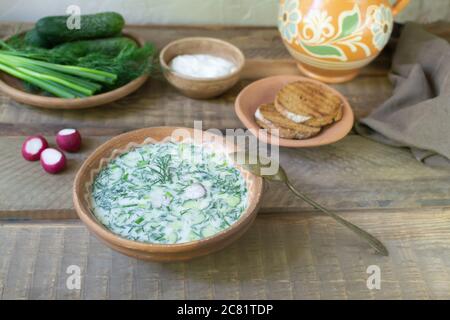 Okroshka, a traditional dish of Russian cuisine. Cold soup in a deep plate with ingredients and an old spoon on a wooden table. Top view. Rustic style Stock Photo