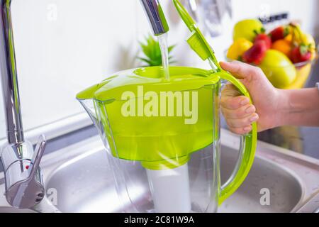 Woman filling water filter jug in the kitchen. Purification and softening of drinking tap water. Closeup Stock Photo