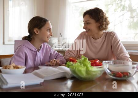 Happy mother and teenager daughter chatting, sitting in kitchen Stock Photo
