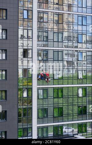 Two industrial climbers from the cleaning service wash the glass facade of a modern high-rise apartment building. Rope access Stock Photo