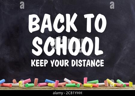 BACK TO SCHOOL KEEP YOUR DISTANCE text message against blackboard with colorful chalks background, Coronavirus spread in school prevention measure Stock Photo