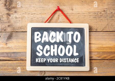 BACK TO SCHOOL KEEP YOUR DISTANCE text message on a blackboard, wooden wall background, Coronavirus spread in school prevention measure Stock Photo