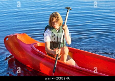 Active happy boy in summer holiday. Teenage school boy having fun enjoying adventurous experience kayaking on lake on a sunny day during summer Stock Photo