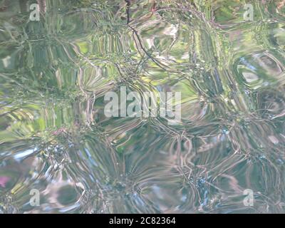 Abstract close-up of the surface of Delapre Lake, where the water is clear as glass, with ripples and reflecting the sunlight. Stock Photo