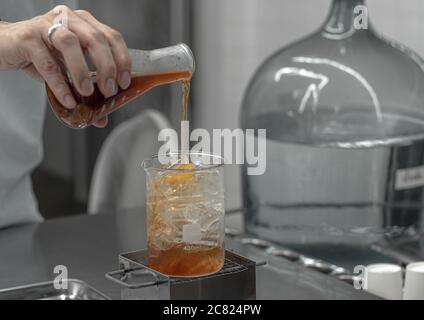 Barista hand holding Lab Borosilicate Glass Beaker Mixing tea drink beverage In Chemistry Bar Beaker Cocktail. Stock Photo