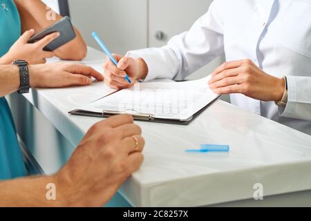 Partial view of doctor in white coat making notes in notepad with female patient near by during appointment in clinic Stock Photo
