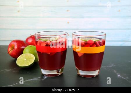 Two Glasses of Red Wine Sangria on the Table with Blurry Apples and Limes in Background Stock Photo