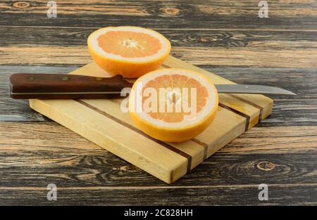 Fresh raw grapefruit halves on wooden cutting board with kitchen knife Stock Photo