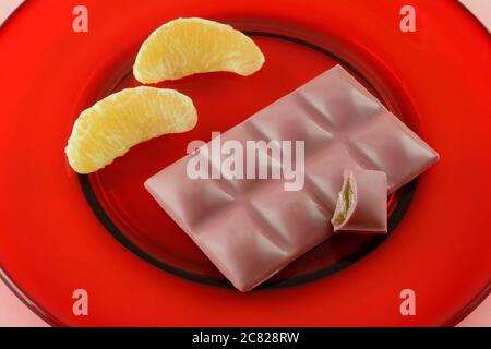 Ruby chocolate candy snack bar with half eaten piece and fresh raw grapefruit sections on red glass plate Stock Photo