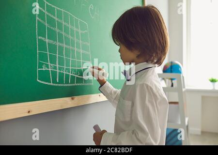 Chess lesson for children. Boy draws a chessboard on the green board in the classroom. Stock Photo