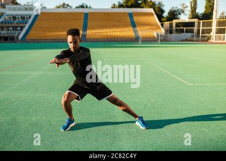 Young attractive African American sportsman doing exercises during workout at stadium Stock Photo