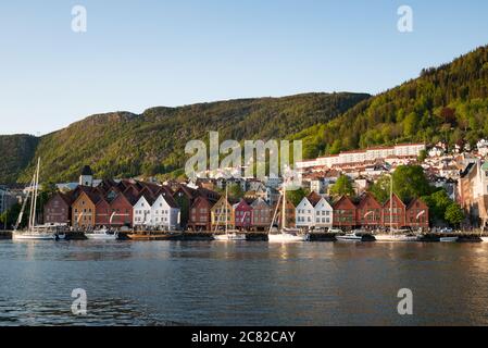 The colourful red, white and burgundy of harbourside Brygge with the tree covered hillside of Floyen behind in Bergen, Norway Stock Photo