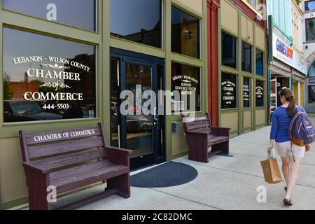 Woman with backpack and shopping bag walking on sidewalk in front of the Lebanon-Wilson County Chamber of Commerce in Lebanon, TN, USA Stock Photo