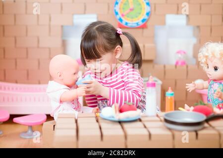 toddler girl pretend play babysitting with baby doll at home Stock Photo