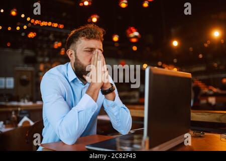 A young caucasian businessman with  hands on his head is sitting in a cafe and working on a laptop. Work in a restaurant Stock Photo