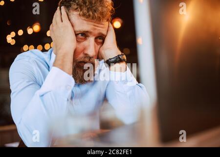 A young caucasian businessman with  hands on his head is sitting in a cafe and working on a laptop. Work in a restaurant Stock Photo