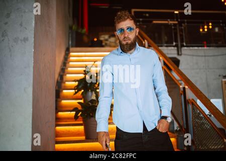 A young caucasian man with sunglasses is standing on the steps in a cafe Stock Photo