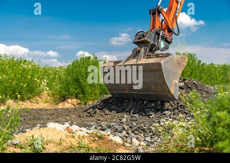 A small excavator is building a new road on a green field. copy space Stock Photo