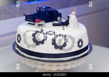 White wedding cake decorated with figures of a black car, the bride and groom Stock Photo