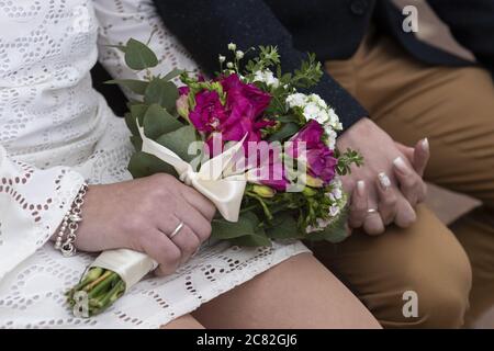 Clasped hands of the bride and the groom with the bride holding a beautiful bouquet Stock Photo