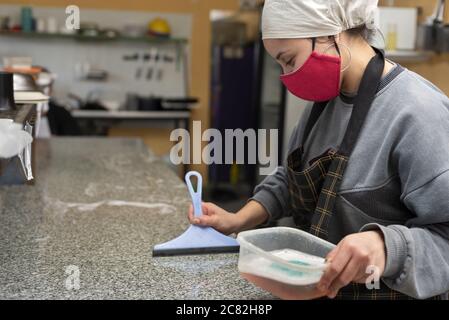 Female wearing a red protective medical face mask and cleaning the table Stock Photo