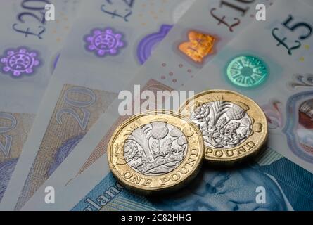 New one pound coins placed on top of new british pound sterling banknotes. Close up photo with selective focus. Main focus is on the coins. Stock Photo