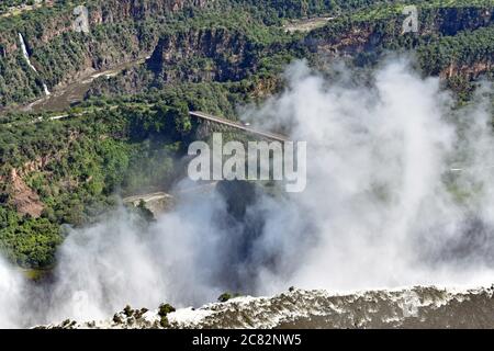 An aerial view of The Smoke That Thunders. Victoria Falls bridge and the gorges can be seen behind the spray from the waterfall.  Zimbabwe and Zambia. Stock Photo