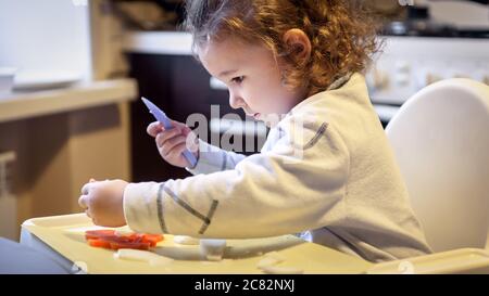 Child cuts carrots and potatoes in kitchen, pretty little girl cooks with toy knife, cute two-year baby plays with eating at home, happy independent k Stock Photo