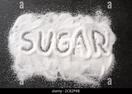 Word SUGAR, written in spilled out sweet crystals on a dark slate, high angle view from above, selected focus Stock Photo