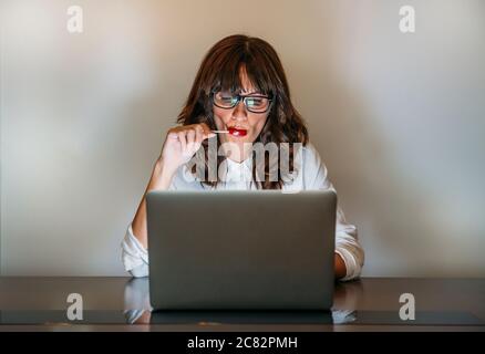 Woman with glasses works with computer and eats a candy Stock Photo