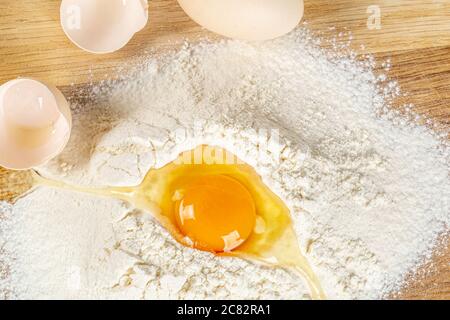 Closeup of a cracked egg on a pile of flour on a wooden surface Stock Photo