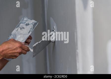 old manual worker with wall plastering tools renovating house. Plasterer renovating indoor walls and ceilings with float and plaster. Stock Photo