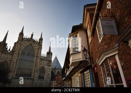 The eastern end of York Minster seen from College Street as the sun begins to set. Tudor style brick buildings overhang the street below. Stock Photo