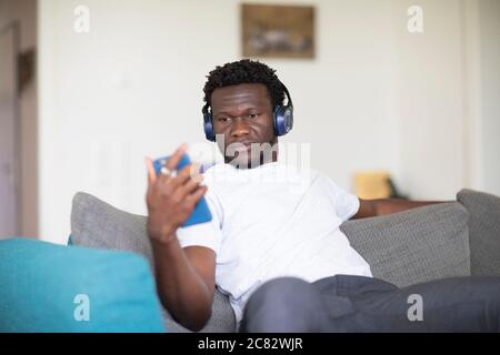 young black man sitting on a couch at home hearing music Stock Photo