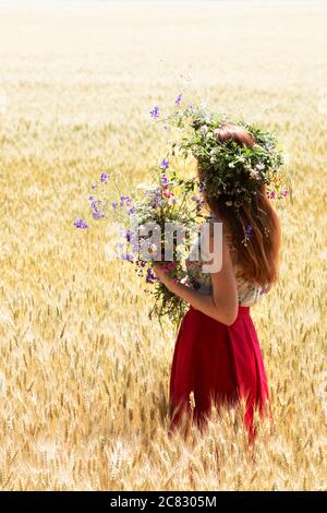 girl in a wreath of wildflowers in a wheat field Stock Photo